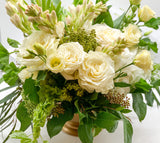 A floral arrangement featuring a mix of white and yellow roses, greenery, and other flowers in a bronze-colored vase.